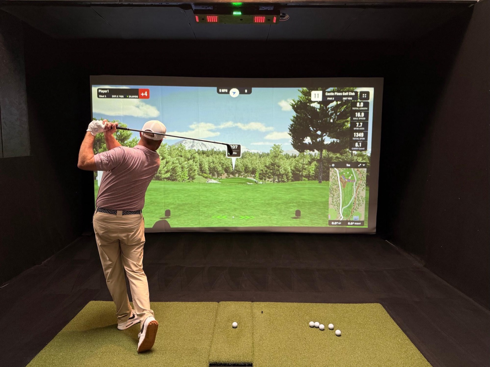 Golfer mid-swing on a Uneekor simulator bay at COR Golf, playing Castle Pines