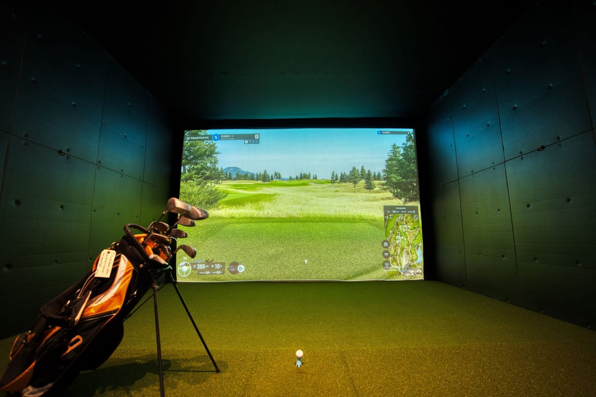 Indoor golf simulator bay with projection screen and hitting mat